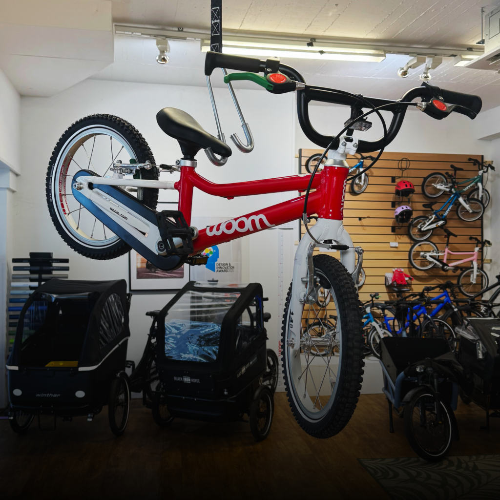 Indoor bike shop display featuring a red-and-white child’s bike in the foreground with other bikes mounted along a wooden wall in the background.
