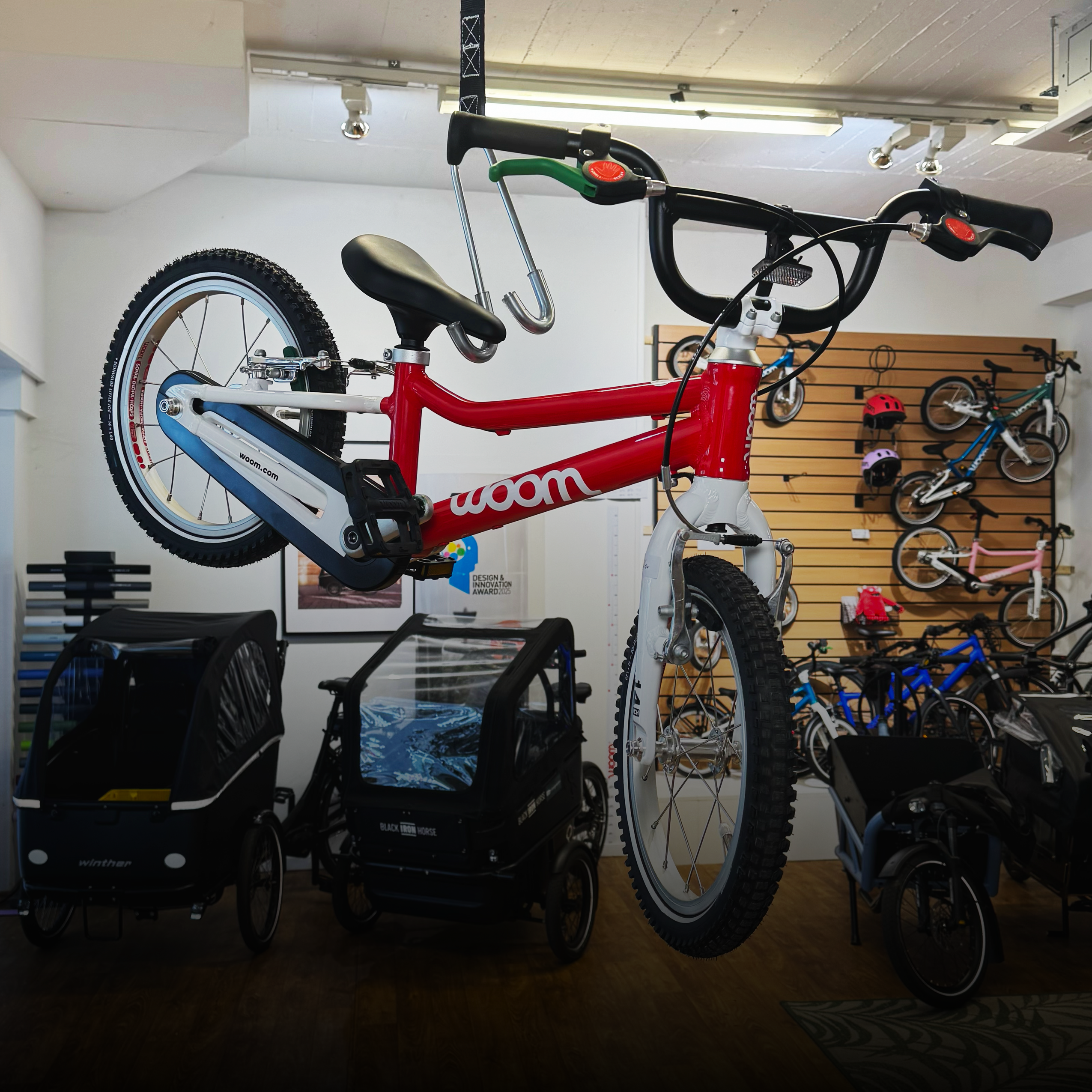 Blog Woom TK V1 - mycargobike köln GmbH Indoor bike shop display featuring a red-and-white child’s bike in the foreground with other bikes mounted along a wooden wall in the background.